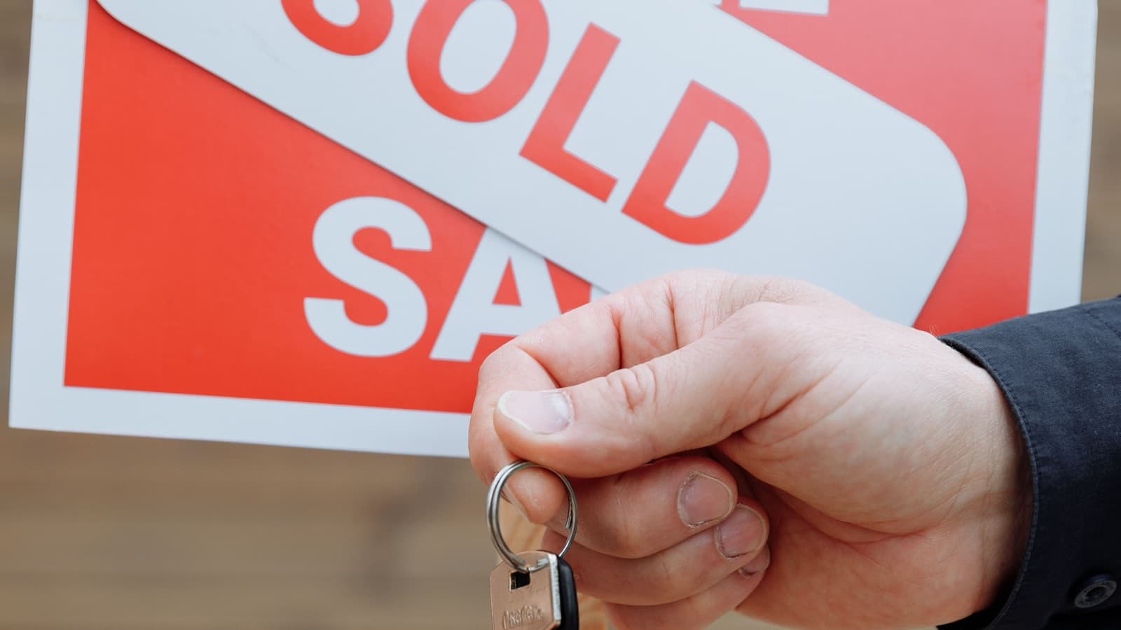 A person handing over house keys in front of a red Sold sign
